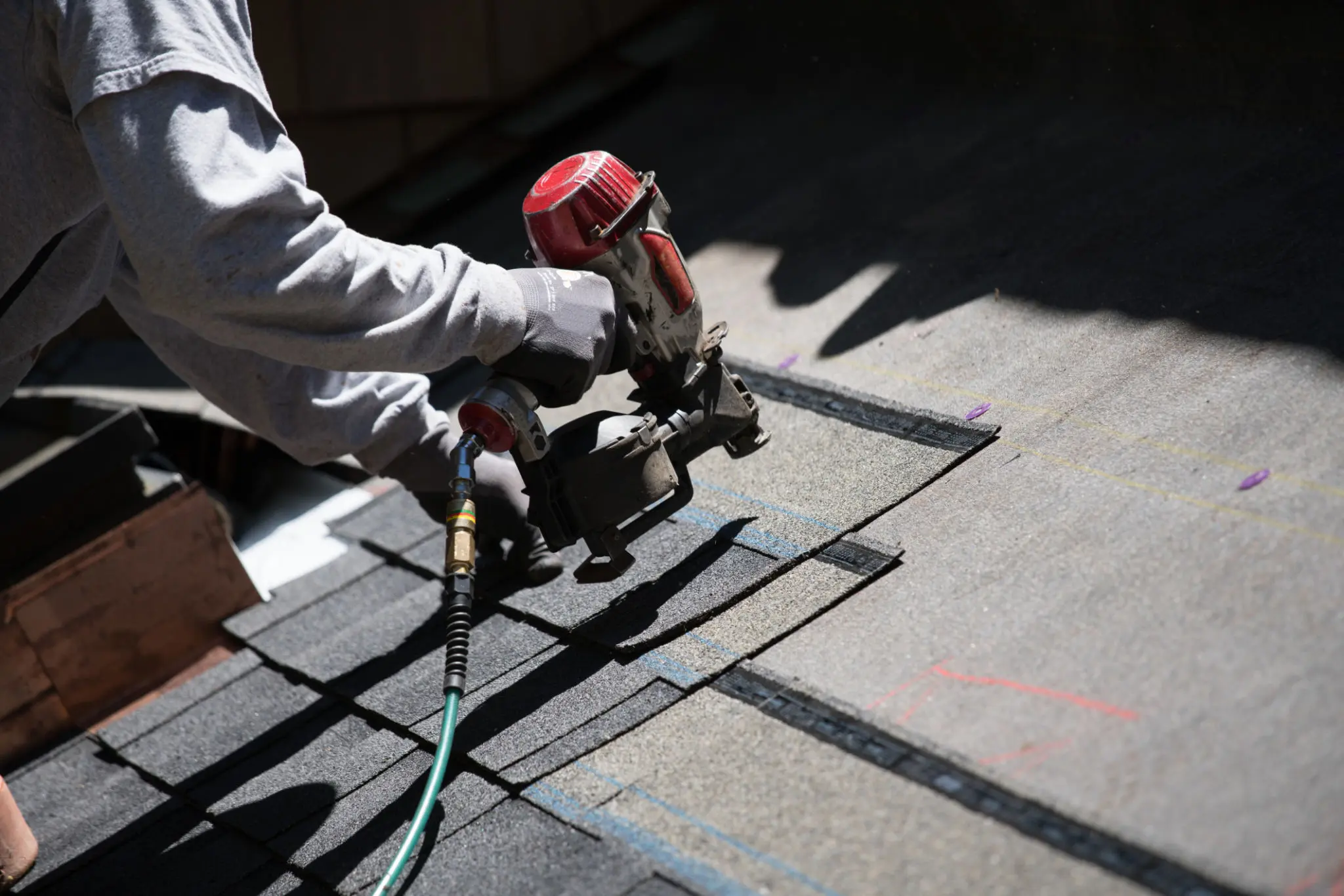 Roofer using nail gun on shingles.