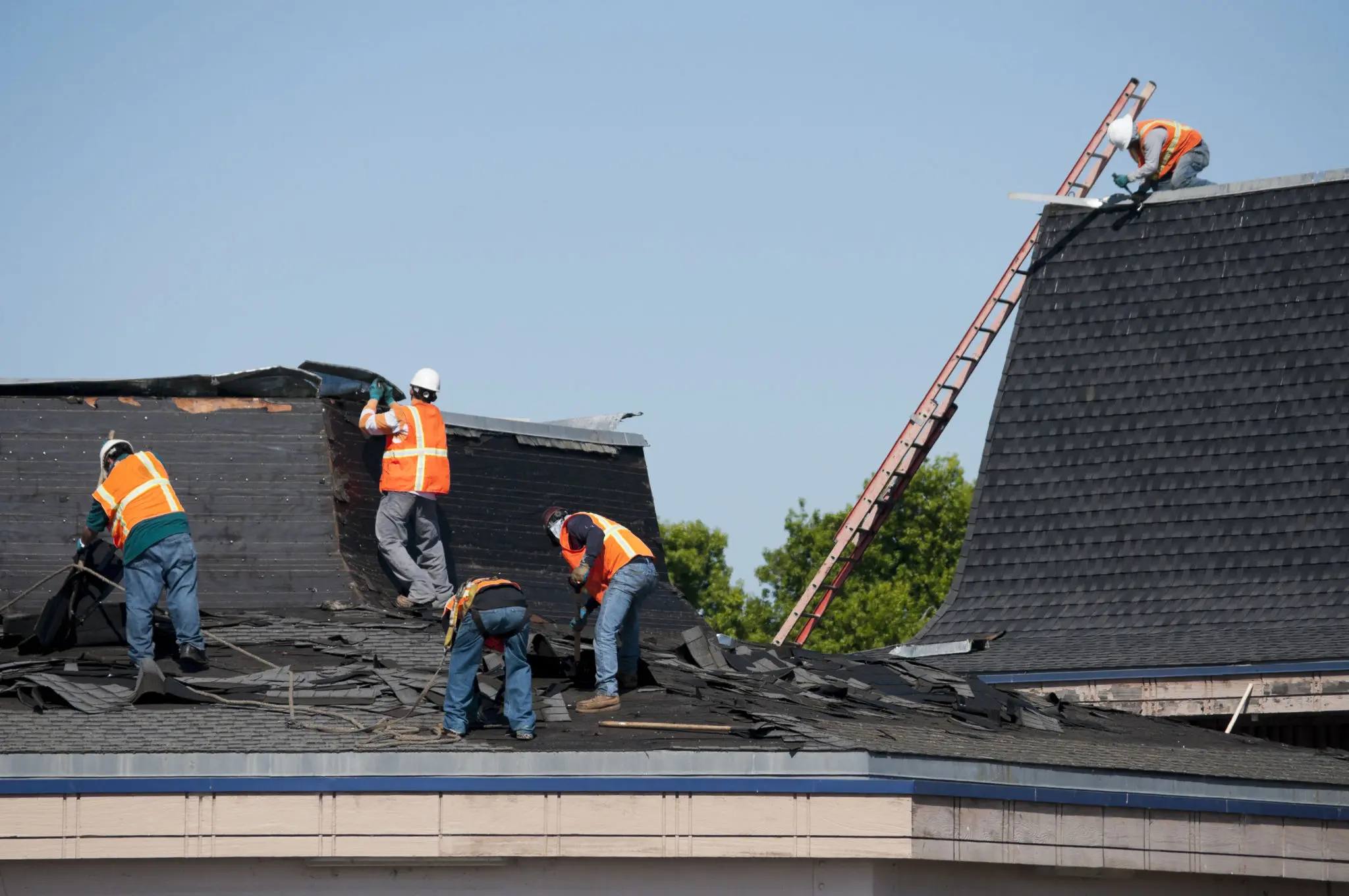 Workers in orange vests repairing a roof.