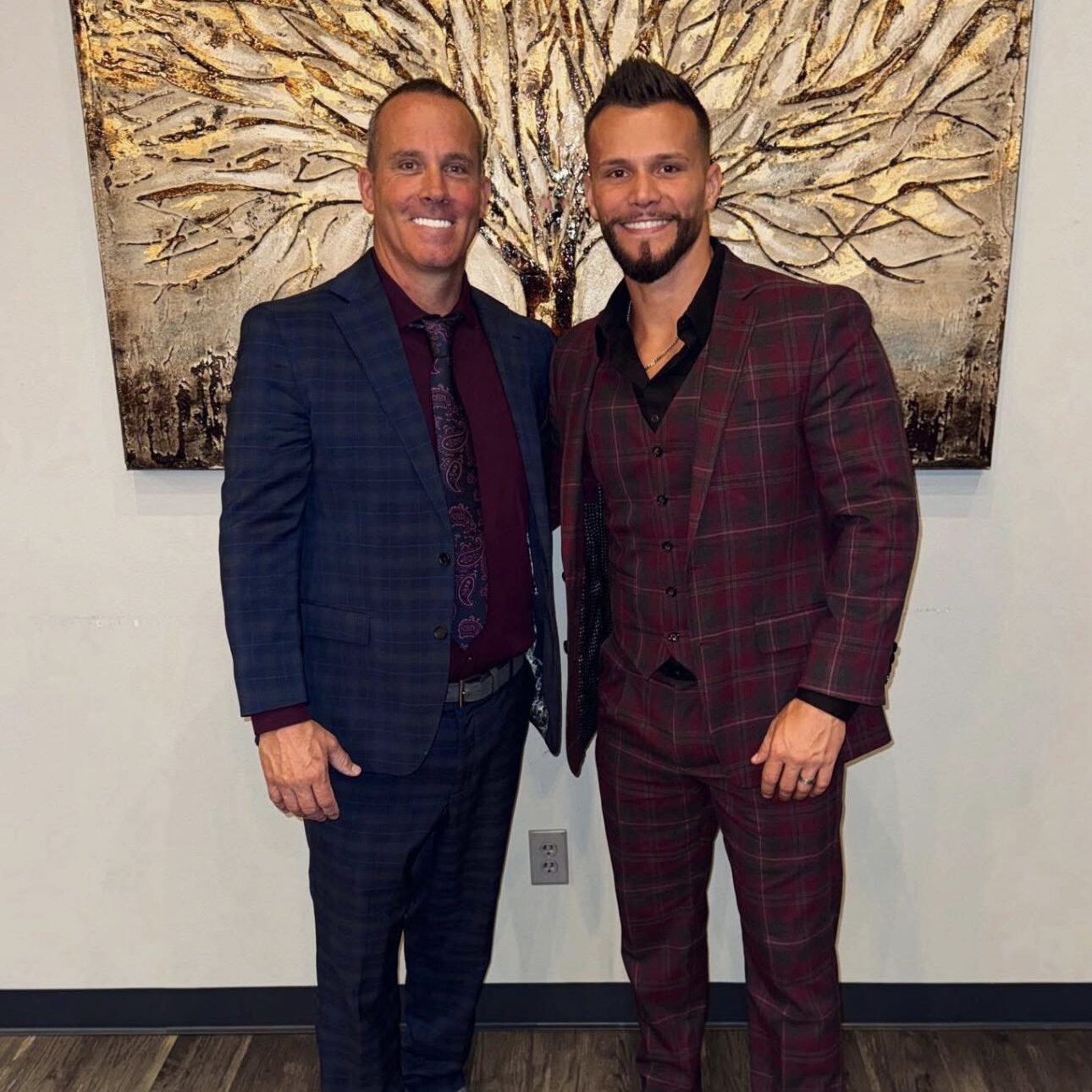 Two men dressed in stylish suits smiling indoors.
